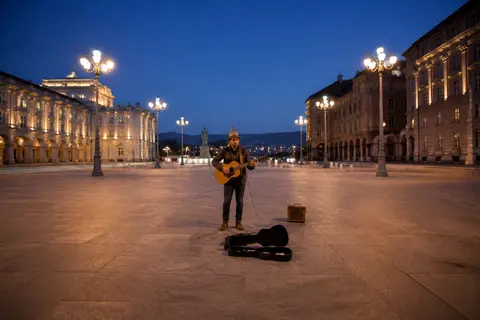 Minh họa cho “quảng trường đô thị”: A street musician in an open urban plaza at blue hour.